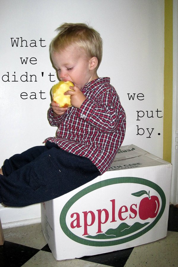 young boy munching on huge apple atop a box labelled "apples" 